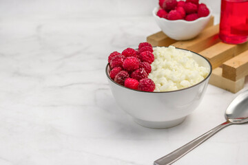Rice porridge with fresh raspberries in a white bowl is on a white table
