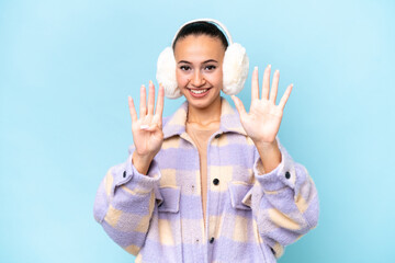 Fototapeta premium Young Arab woman wearing winter muffs isolated on blue background counting nine with fingers