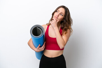 Young sport caucasian woman going to yoga classes while holding a mat isolated on white background having doubts