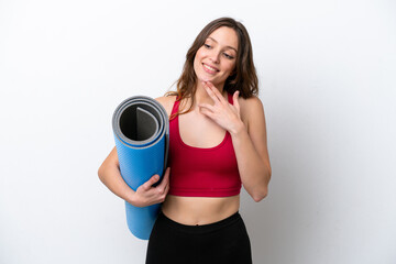 Young sport caucasian woman going to yoga classes while holding a mat isolated on white background looking up while smiling