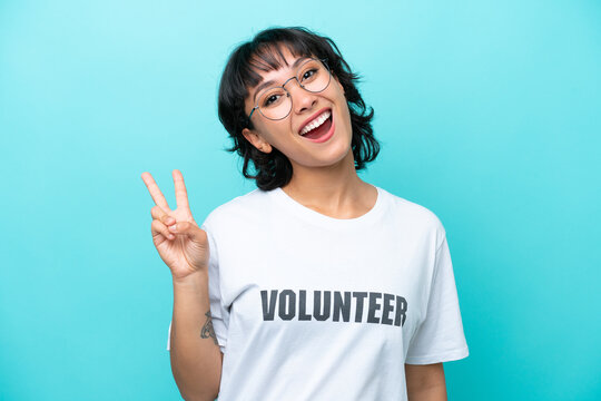 Young volunteer Argentinian woman isolated on blue background smiling and showing victory sign