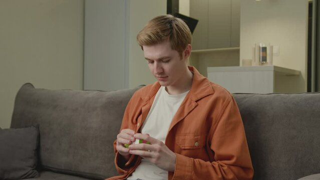 Man Solving Cube Jigsaw Sitting on Couch. Smart young adult plays with cube puzzle at home. Brain training puzzle.
