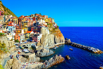 Colorful Cinque Terre village of Manarola, Italy. View of the harbor with boats in the blue sea.