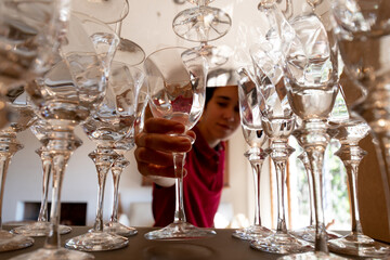 Joven ordenando una vitrina con copas de cristal, con enfoque selectivo en primer plano y...