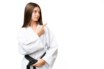 Teenager girl over isolated chroma key background doing karate and pointing to the lateral