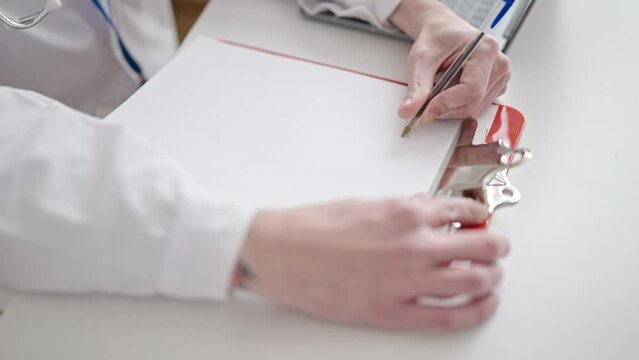 Young hispanic man doctor writing on clipboard at clinic