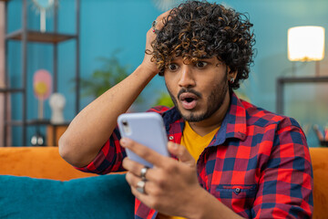 Sad displeased indian man use smartphone typing browsing, loses becoming surprised sudden lottery...