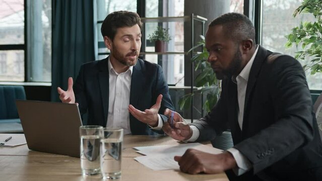 Two diverse businessmen multiracial partners with documents laptop at office meeting. Caucasian male business expert salesman man explain software consulting African American client customer investor