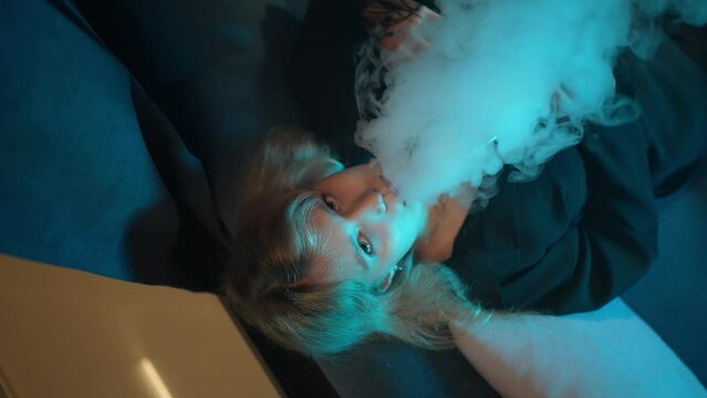 Young sexy girl smokes hookah and lets out steam