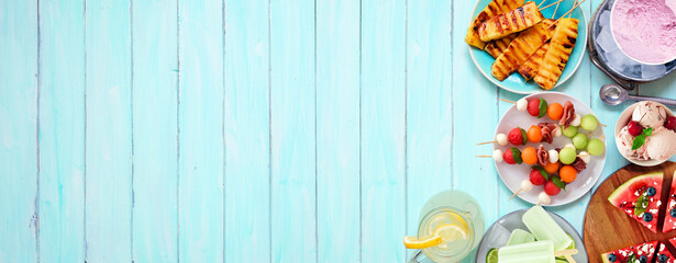 Refreshing summer food side border. Selection of grilled fruits, ice cream and ice pops. Top view on a blue wood banner background.