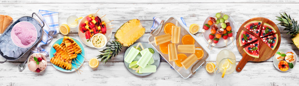 Refreshing summer food table scene. Assorted grilled fruits, ice cream and ice pops. Overhead view on a white wood banner background.
