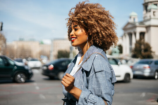 Beautiful And Confident Black Woman Walking Down The Street. She Is Happy And Smiled. Bright Sunny Day. Side View.