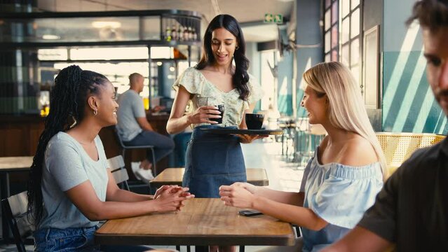 Woman meeting friend in coffee shop paying bill with contactless mobile phone payment - shot in slow motion