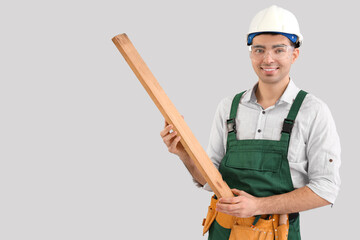 Young carpenter with wooden plank on grey background