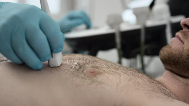 Ultrasound: doctor checks the man's thoracic cage with an ultrasonography machine. Diagnosis of heart and vascular diseases. Screening of the body in the clinic office. Sonograms health check
