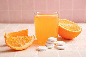 Glass of vitamin C effervescent tablet dissolved in water and orange on tiled table