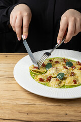 A plate of ravioli with green sauce and basil leaves on a wooden table.