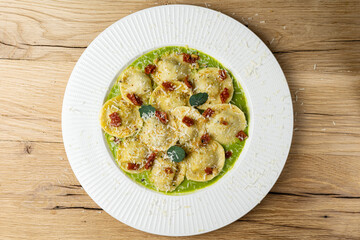 A plate of ravioli with green sauce and basil leaves on a wooden table.