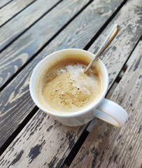 A cup of coffee standing on a wooden brown table.