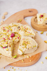 Wooden board of tasty Tahini halva with pistachios on light background