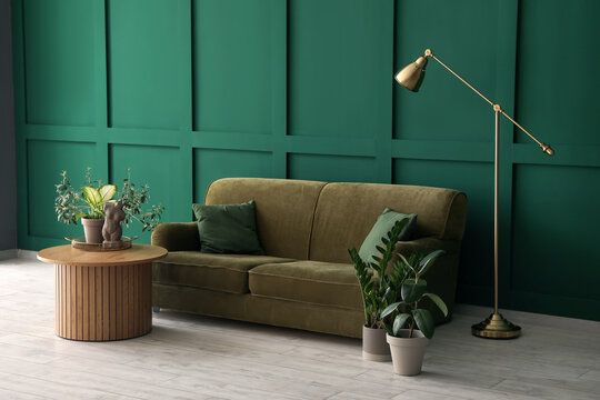 Cozy sofa, lamp and coffee table with woman figurine near green wall