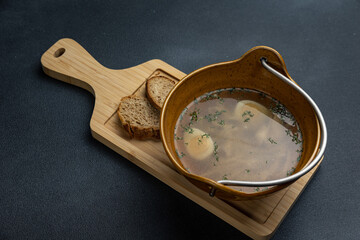 A bowl of soup with two pieces of bread on a wooden board.