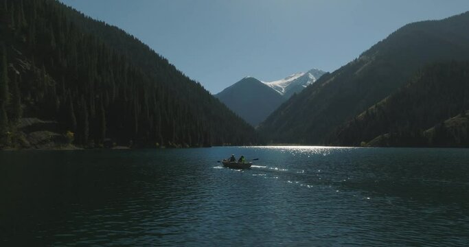 Twosome sail on the boat on deep mountain Lake Kolsai. Lifestyle outdoors nature tourism. Beautiful landscape of mountain nature reserve. Aerial drone view with snow peak mount background.