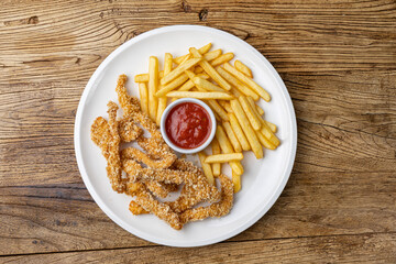 A plate of chicken nuggets with french fries and ketchup on a wooden table.