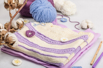 Fototapeta na wymiar Handmade crocheted baby t-shirt in lilac tones. Stuff contains thread, hooks, knitting needles