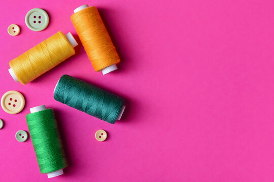 Colorful thread spools and buttons on pink background