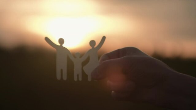 Selective focus of male hand holding paper family cutout on background calm sunset, foster care, homeless support, world mental health day. Autism support, homeschooling education, parents day concept