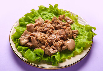 Plate with delicious canned tuna and fresh lettuce on lilac background