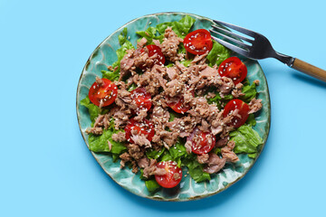 Plate with delicious tuna salad and fork on blue background