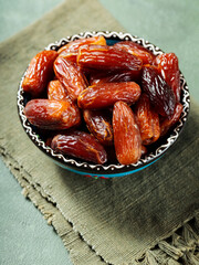 Bowl of pitted dates on a green linen napkin. Tasty sweet dried dates in bowl on a green background. Ramadan kareem
