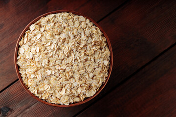 Oat flakes in a clay bowl on a wooden background. Dry rolled oatmeal on wooden boards. Copy space