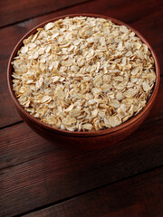Oat flakes in a clay bowl on a wooden background. Dry rolled oatmeal on wooden boards. Copy space