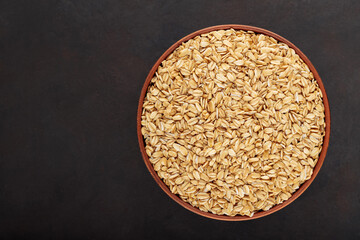 Oat flakes in clay bowl on a dark background. Raw oatmeal for healthy nutrition. Top view. Copy space