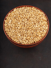Oat flakes in clay bowl on a dark background. Raw oatmeal for healthy nutrition. Top view. Copy space