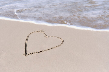 Wave running to heart shape drawn on white sand of tropical beach.