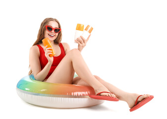 Beautiful young woman with sunscreen creams and inflatable ring on white background