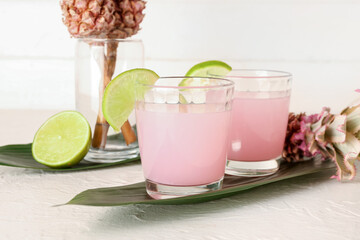 Glasses of cocktail with lime, baby pineapples and palm leaves on white table, closeup