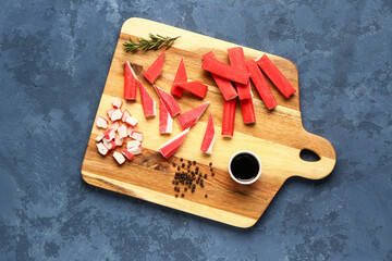 Wooden board with tasty crab sticks and sauce on blue background © Pixel-Shot