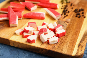 Wooden board with tasty crab sticks on blue background, closeup