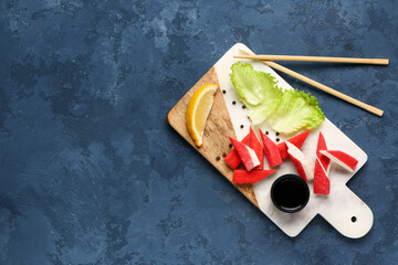 Board with tasty crab sticks and sauce on blue background © Pixel-Shot