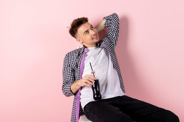 A happy young man sitting with a bottle of coke. fast food and sugar addiction. Isolated on pink background.