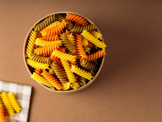 Three colors fusilli pasta on a linen napkin. Green, orange and yellow fusilli pasta stored in eco box. Copy space