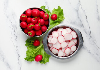 Bowls with fresh slices of radish and lettuce on marble background