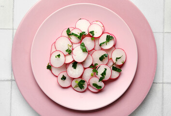 Plates with fresh slices of radish on light tile background