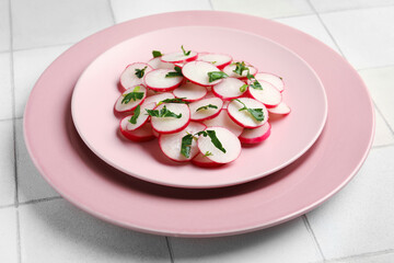 Plates with fresh slices of radish on light tile background