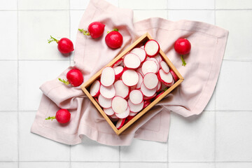 Fresh slices of radish in wooden box on light tile background